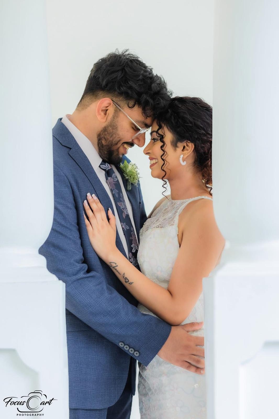Amanda and Shanuka forehead to forehead between white columns